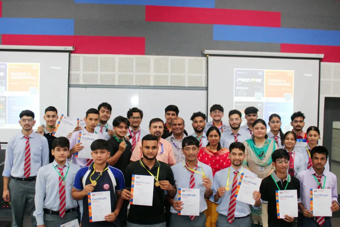 Group of students and teachers in a classroom posing with certificates after a ceremony, smiling for the camera.