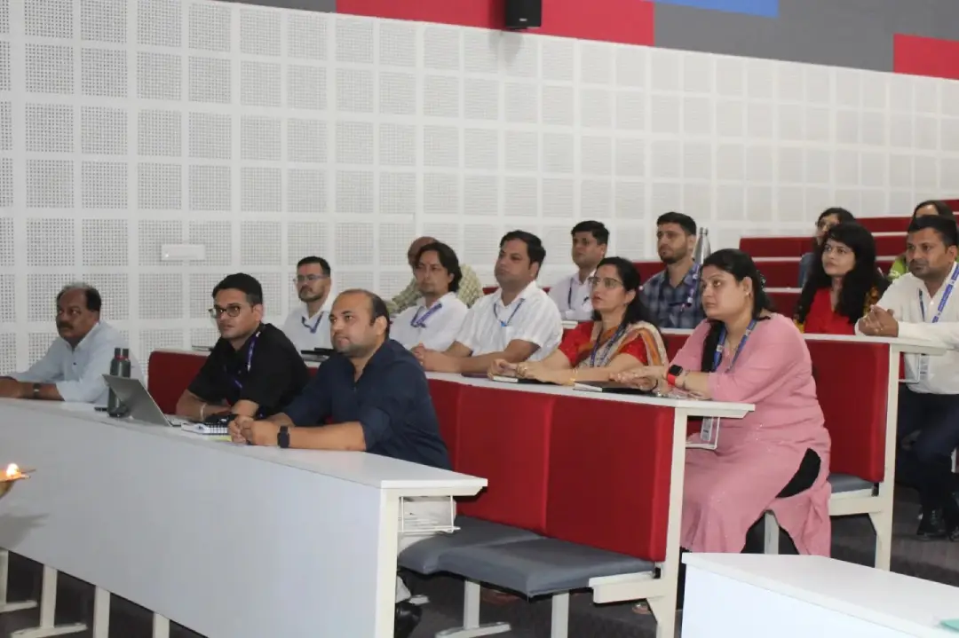 Group of adults seated in a lecture hall, attentively listening with notebooks and lanyards on their necks.