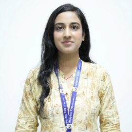 Portrait of a woman with long dark hair wearing a beige patterned kurta and a blue lanyard, facing the camera.