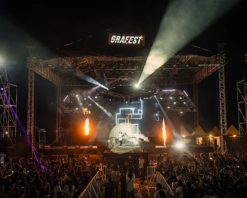 Nighttime Graefest concert with a lit stage, spotlights, flames, and a cheering crowd in front of the stage.