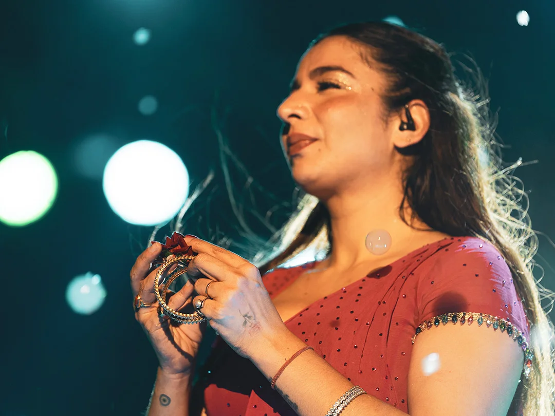 Female singer on stage smiling, holding a tambourine, in a red beaded dress with in-ear monitor.